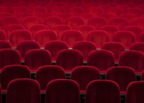 Rows of empty red velvet theater seats in an auditorium.