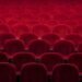 Rows of empty red velvet theater seats in an auditorium.