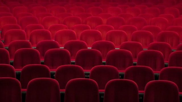 Rows of empty red velvet theater seats in an auditorium.